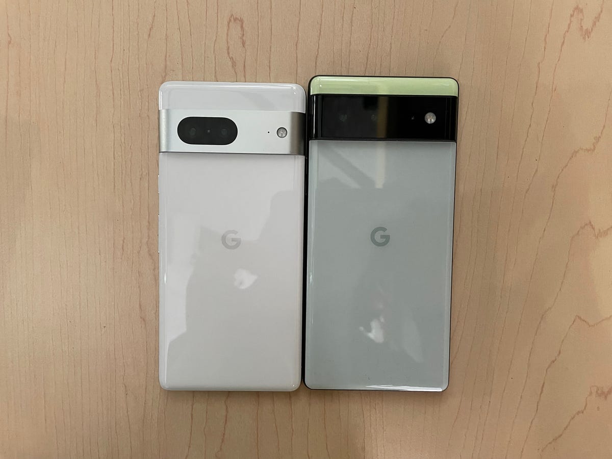 Google's Pixel 7 (next) to the left of the Pixel 6 (right) on a wooden background